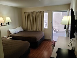 Ein Hotelzimmer mit zwei Betten, einem Schreibtisch, einem Stuhl und einem Vorhangfenster.