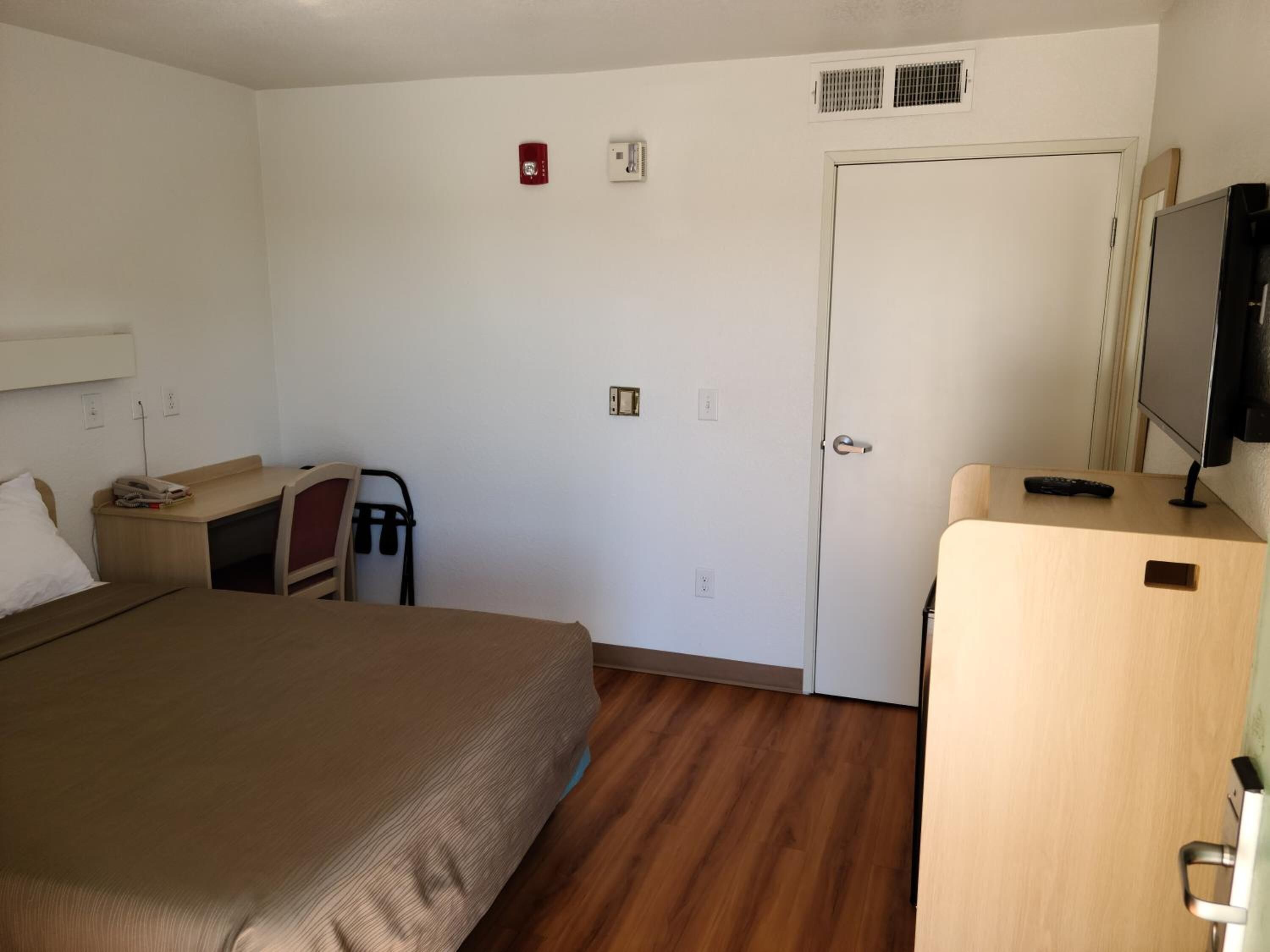 Una habitación de hotel con cama, escritorio, silla, televisor y puerta.