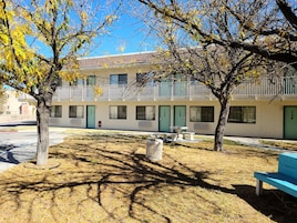 A building with multiple rooms, each with a door and windows, and a small outdoor seating area with tables and benches.