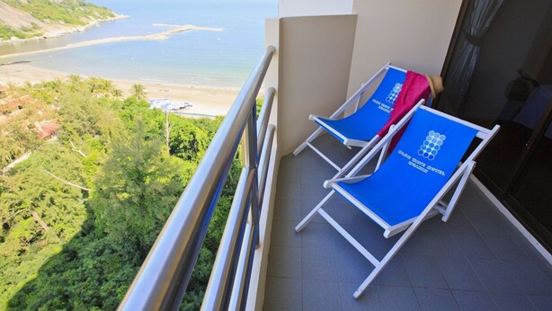 A balcony with two blue lounge chairs, one with a pink towel, overlooking a beach and greenery.