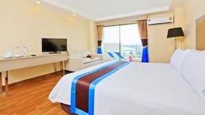 A hotel room with a bed, a desk with a television, a chair, and a window with curtains.