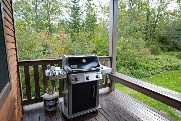 A barbecue grill on a wooden deck with a view of a forest. - Riverfront Cabin|Fireplace|Fire pit | White Mountains| Hiking (Twin Mountain)