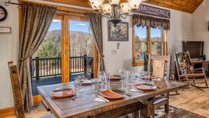 A dining area with a wooden table set for four, a chandelier, and a view of mountains through large windows.