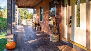 A wooden porch with a welcome mat, a bear statue, and a door with a window.