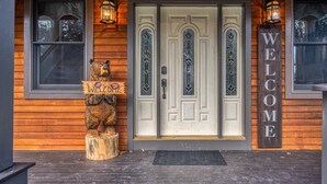 A wooden building with a white door, two lanterns, a 'WELCOME' sign, and a bear statue.