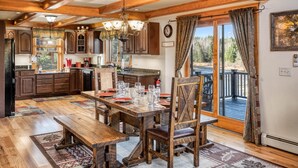 A rustic kitchen with wooden cabinets, a dining table set for four, and a large window overlooking a deck.