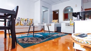 Un salon moderne avec un plancher en bois, un ensemble de canapés, une table à manger et un tapis à motifs.