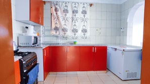 Une cuisine de taille réduite, équipée d’une cuisinière, d’un four à micro-ondes et de meubles de rangement rouges.