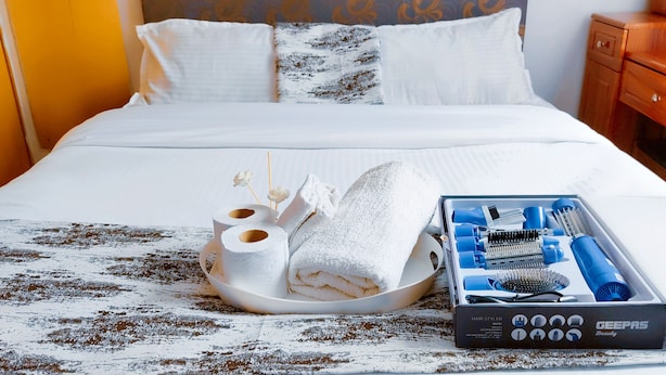 Un lit bien fait, avec du linge de lit blanc, un plateau contenant des serviettes et des articles de toilette, et une trousse de coiffure posée sur le lit.