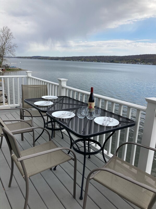 A deck with a table set for dining, overlooking a lake. - Relax lakeside at our spacious Geneseo house on Conesus Lake (Conesus)