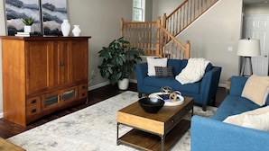 A living room with a wooden cabinet, a blue sofa, a coffee table, and a staircase. - Relax lakeside at our spacious Geneseo house on  Conesus Lake (Conesus)