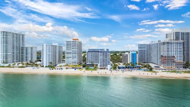 Un paysage urbain côtier avec de hauts immeubles, une plage de sable et un ciel bleu dégagé.
