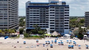 Un hôtel situé en bord de mer, avec plusieurs étages, une piscine et des parasols sur la plage.