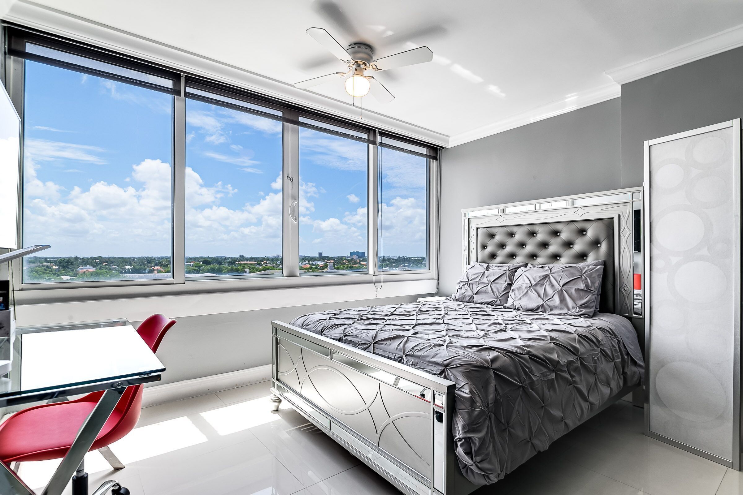 Un dormitorio con cama, escritorio, silla y un amplio ventanal con vistas a la ciudad.