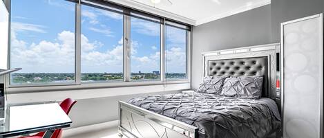 Un dormitorio con cama, escritorio, silla y un amplio ventanal con vistas a la ciudad.