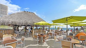 Un espace extérieur aménagé avec des tables et des chaises, une structure à toit de chaume et des parasols.