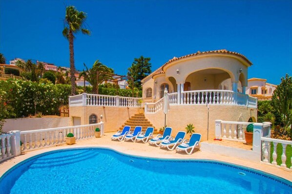 A swimming pool with lounge chairs, a building with a balcony, and a clear blue sky. - Home SEA&DREAMS NiceView II (Calpe)