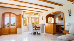 A spacious living area with wooden beams, a dining table with chairs, and a kitchen area with wooden cabinets. - Home SEA&DREAMS NiceView II (Calpe)