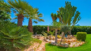 A garden with palm trees, a stone wall, and a well-maintained lawn. - Home SEA&DREAMS NiceView II (Calpe)