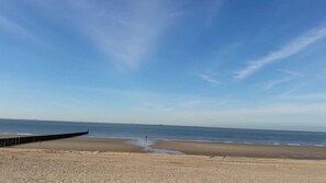 A beach with a wooden jetty extending into the water, a clear sky, and calm sea.