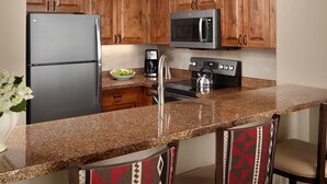 A kitchen with wooden cabinets, a stainless steel refrigerator, a microwave, a stove, and a coffee maker. - Ski Resort (Vail)
