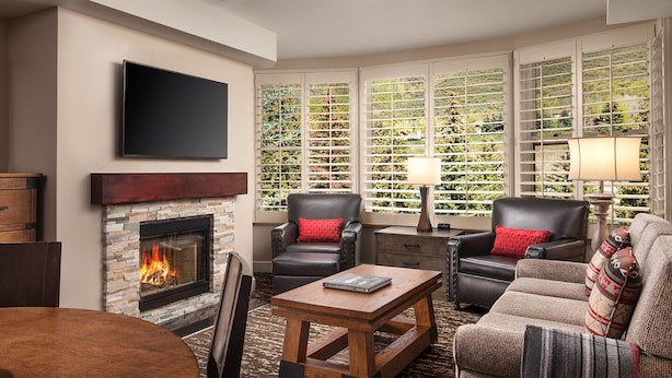 A living room with a stone fireplace, leather sofas, a coffee table, and a TV mounted on the wall. - Ski Resort (Vail)