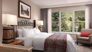 A hotel room with a large bed, two bedside lamps, a framed picture on the wall, a window with a view of trees, and a chair with a red cushion. - Ski Resort (Vail)
