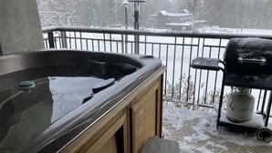 A hot tub on a balcony with a view of a snowy landscape and a grill.
