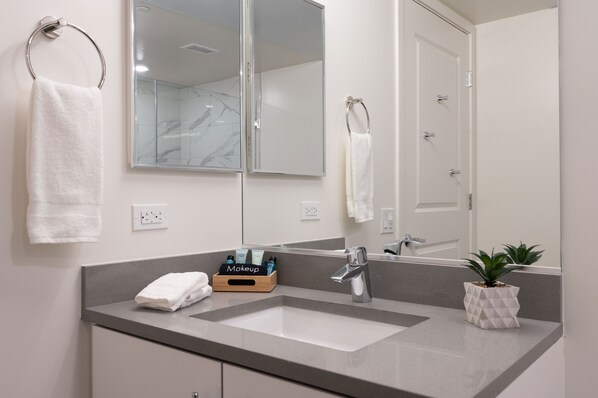 Une salle de bain avec un lavabo, un miroir, un porte-serviettes et une petite plante.