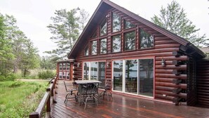 A log cabin with a deck, large windows, and a view of the surrounding forest.