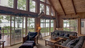 A spacious room with large windows overlooking a lake, furnished with a sofa, chairs, and a table.