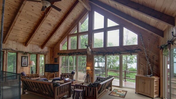 A spacious living area with a high ceiling, large windows, and a fireplace.