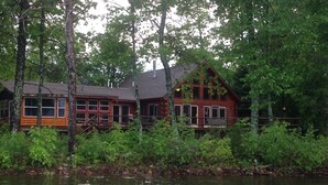 A cabin with a dock extending into a lake, surrounded by dense greenery.