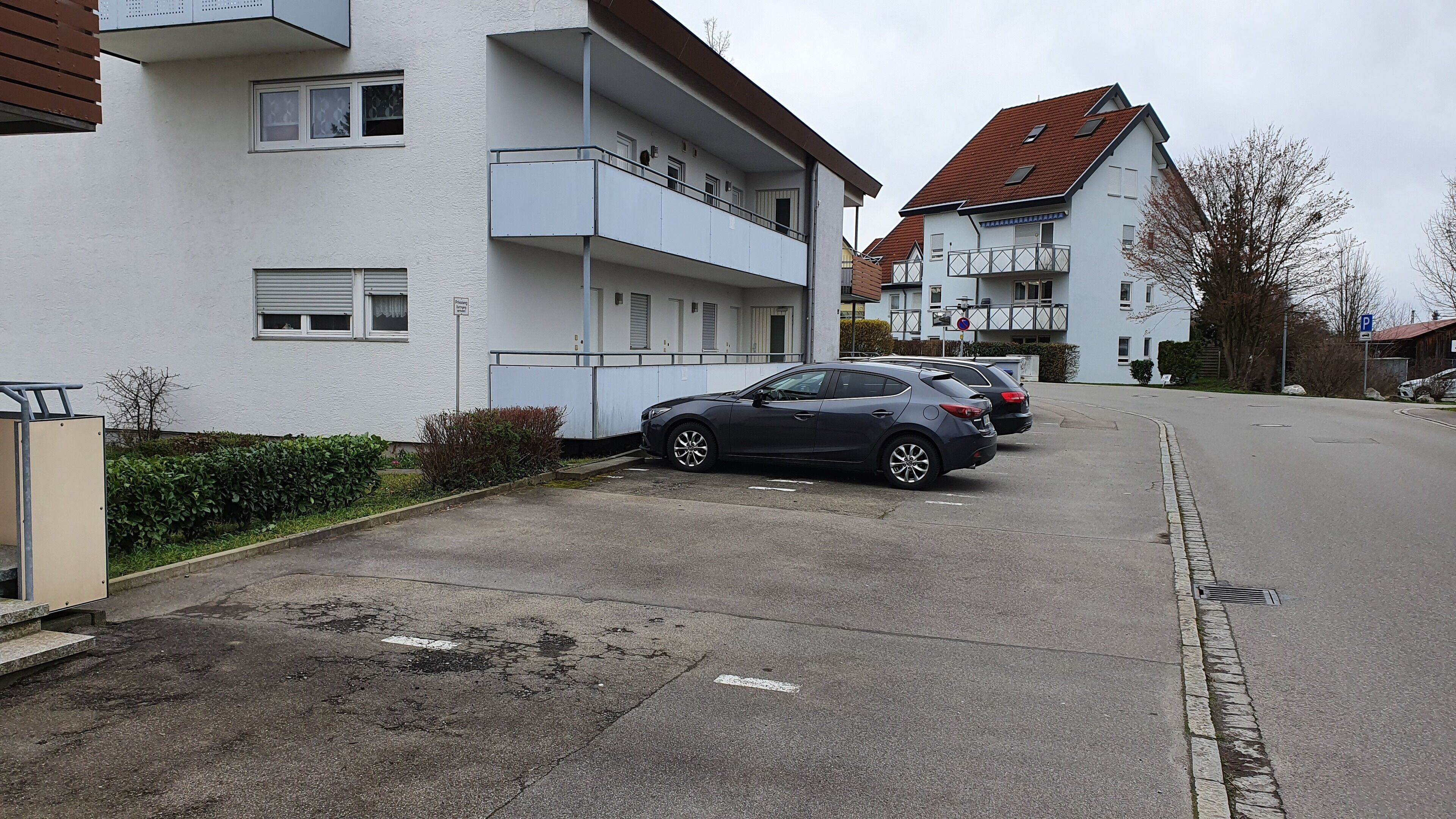 Eine Wohnstraße mit mehrstöckigen Wohngebäuden, einem Parkplatz und parkenden Autos entlang der Seite.