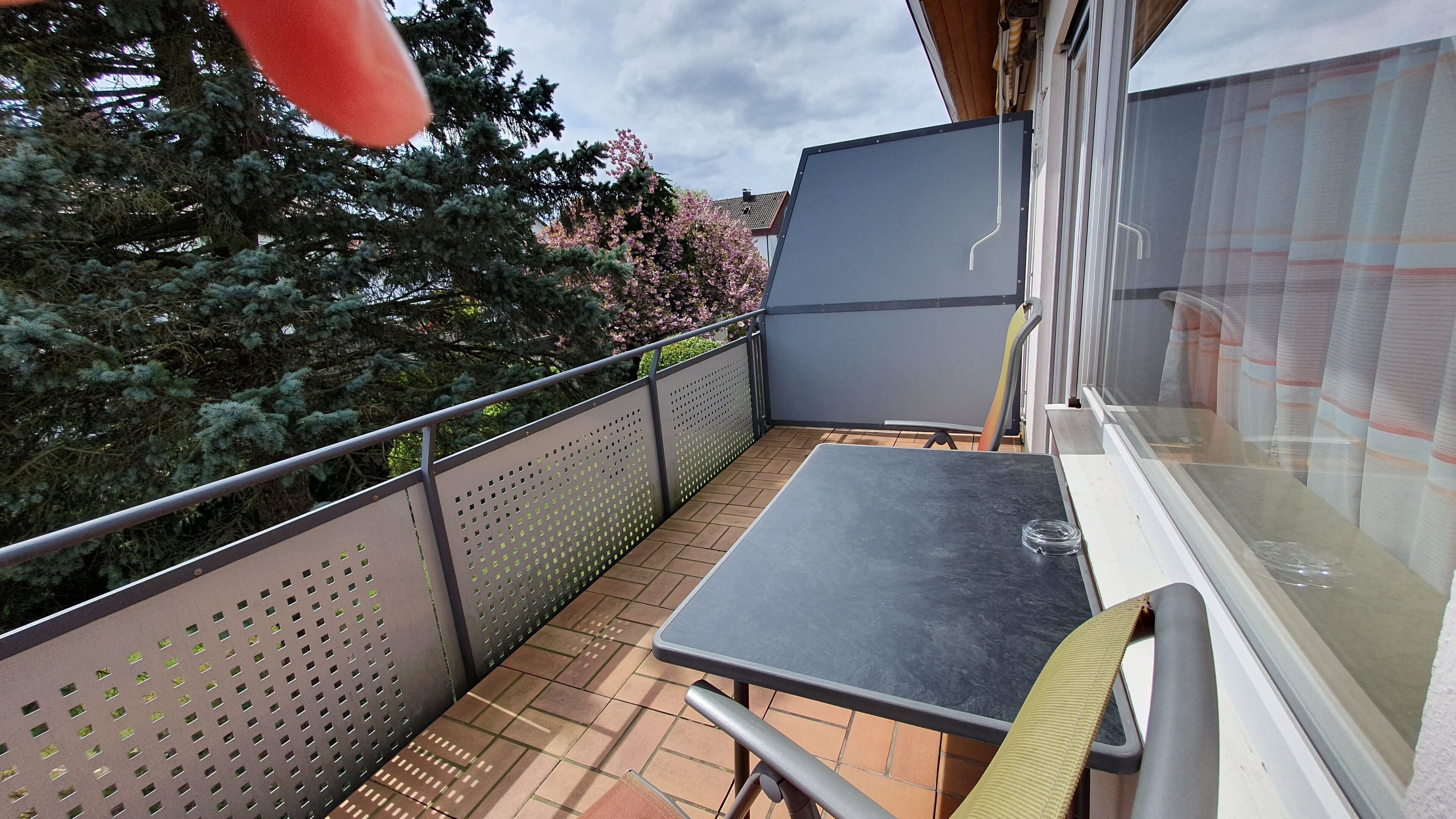 A balcony with a table and chairs, a metal fence, and a view of trees and a building.
