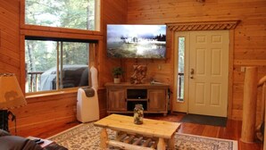 A wooden cabin interior with a television mounted on the wall, a wooden bench, and a door. - Mountain Pines Luxury Yellowstone Cabin + Hot Tub + Sleeps 15 + Garage + 2 Acres (Island Park)