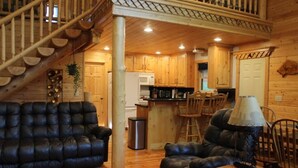 A wooden interior with a staircase, a black leather sofa, a dining area, and a kitchen. - Mountain Pines Luxury Yellowstone Cabin + Hot Tub + Sleeps 15 + Garage + 2 Acres (Island Park)