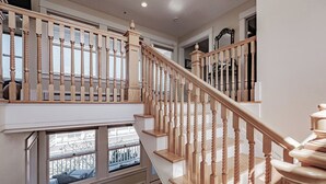 A multi-level wooden staircase with a handrail, leading to a landing with a window overlooking a cityscape.