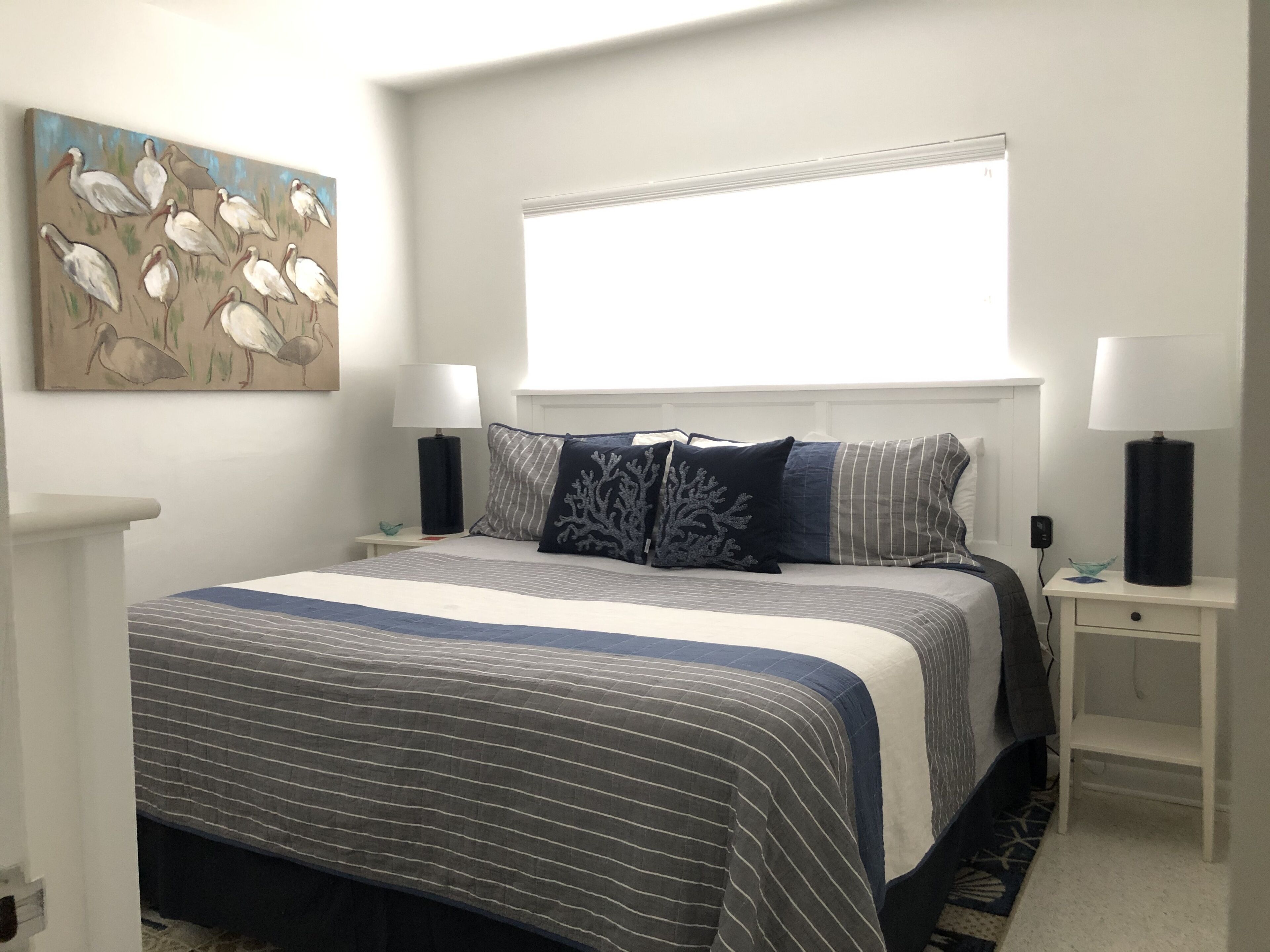 A bedroom with a large bed, two bedside tables, a window, and a painting on the wall.