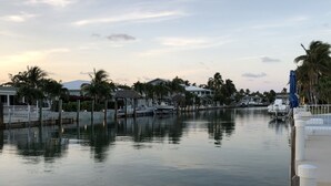 Ruhige Uferpromenade mit vertäuten Booten, Palmen und Häusern entlang des Strandes.