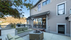 A patio with outdoor furniture, a fire pit, and a house with large windows and a deck. - Old Town Private Home by Luxury Mountain Destinations (Park City)
