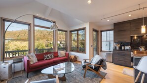 A modern living room with a red sofa, a glass coffee table, and a view of a hillside. - Old Town Private Home by Luxury Mountain Destinations (Park City)