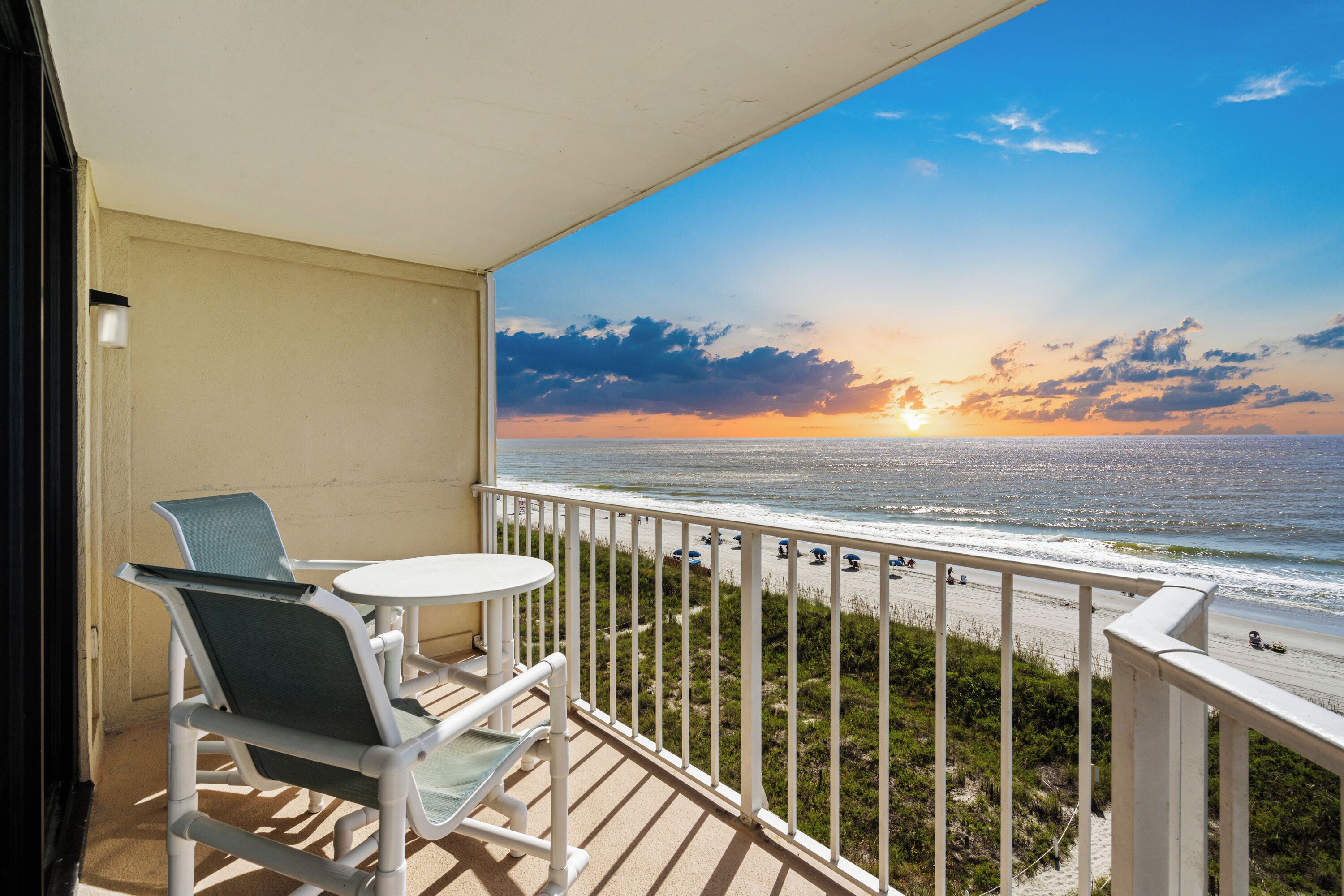 Ein Balkon mit Blick auf das Meer bei Sonnenuntergang, ein weißer Tisch und zwei Stühle.