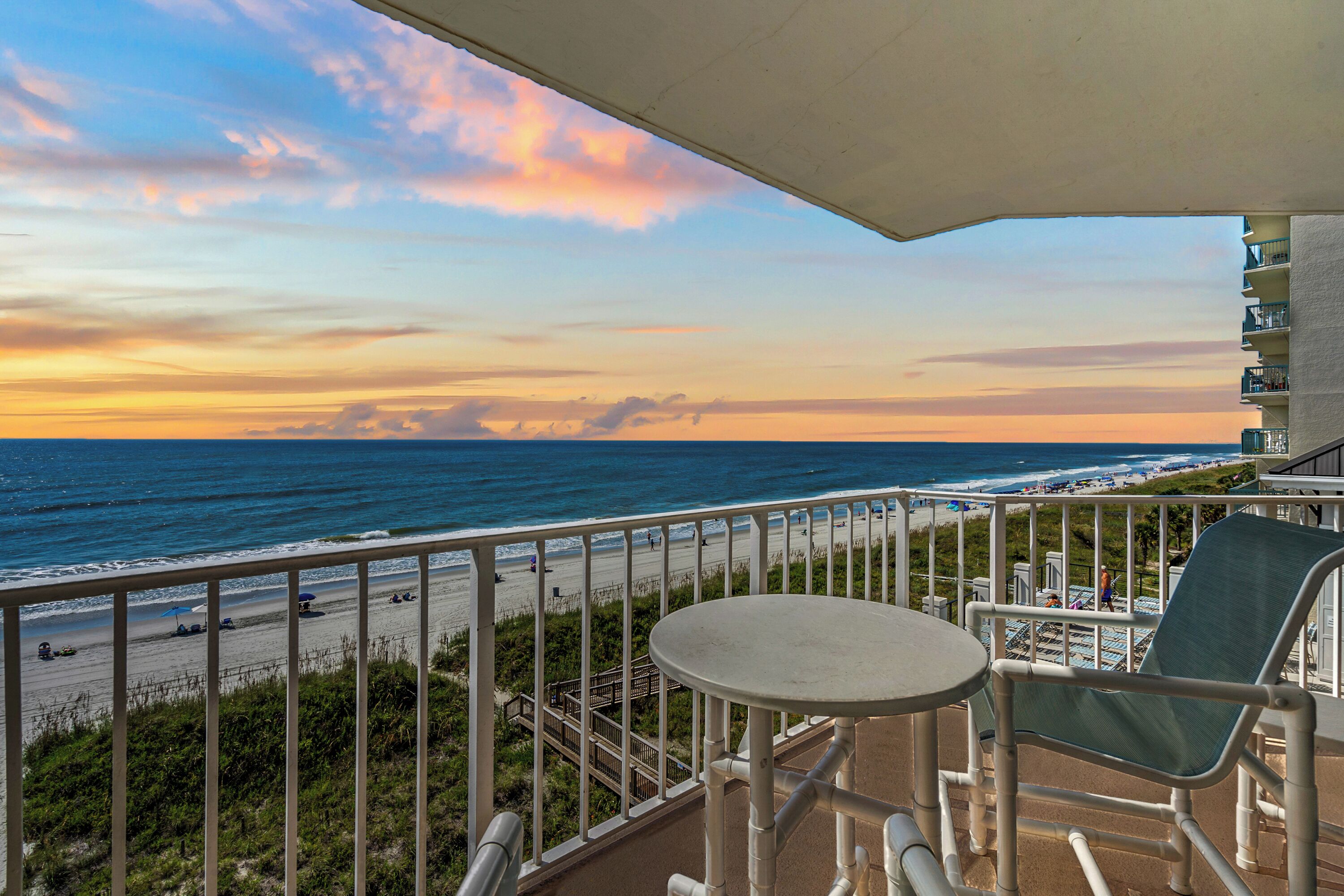 A balcony with a view of the beach and ocean at sunset.