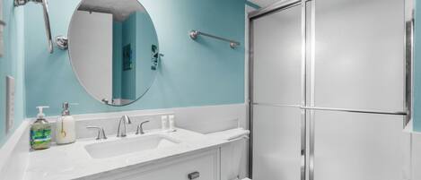 A bathroom with a white sink, a mirror, and a shower enclosure.