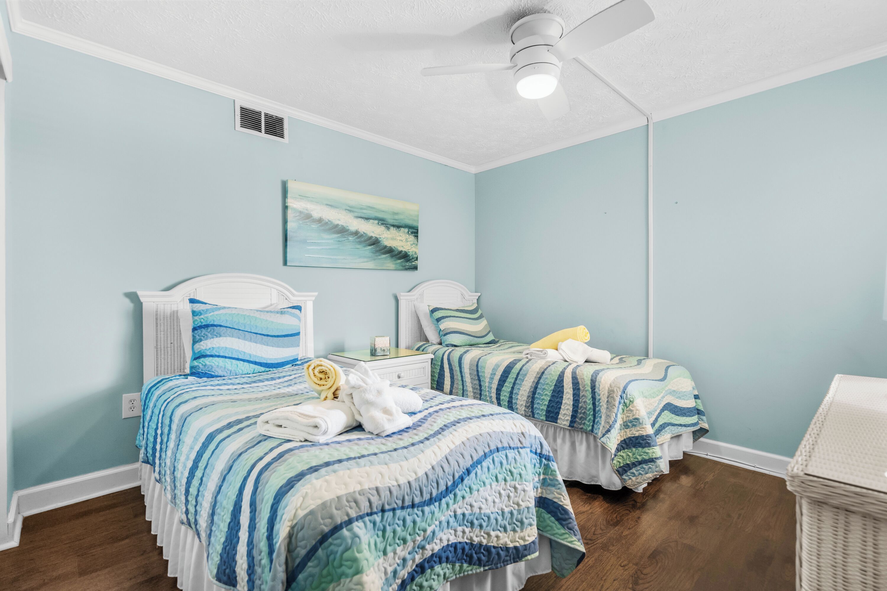 A bedroom with two beds, a ceiling fan, and a painting on the wall.
