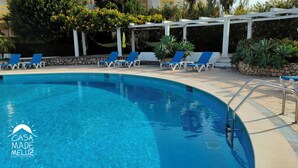 Ein Swimmingpool mit blauem Wasser, umgeben von blauen Liegestühlen und einer weißen Pergola.