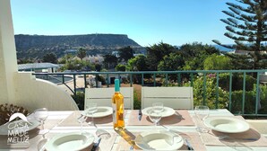 Ein Tisch für zwei, gedeckt mit Wein, Tellern und Besteck, mit Blick auf eine schöne Hügellandschaft und Küste.