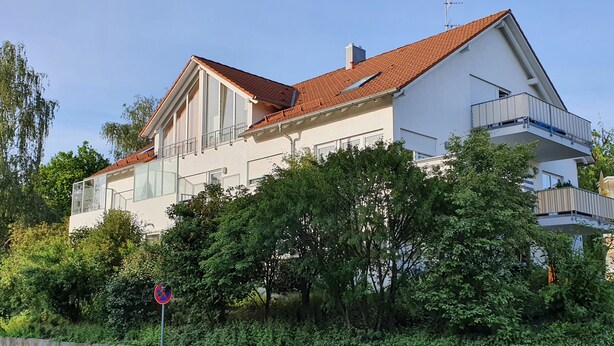 Ein modernes, zweistöckiges Haus mit rotem Ziegeldach, großen Fenstern und einem Balkon.