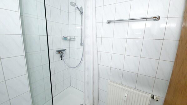 Un baño pequeño con azulejos, ducha, toallero y radiador.